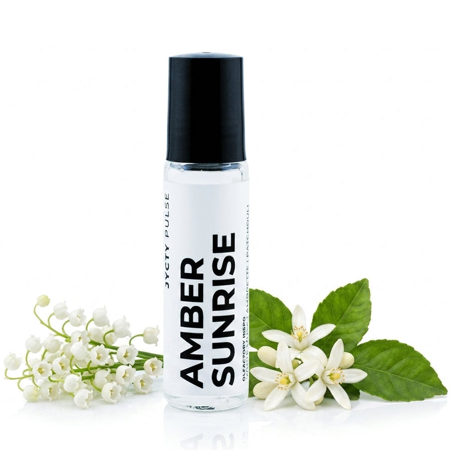 A clear cylindrical roller bottle with a black cap and a white label reading 'JYCTY PULSE AMBER SUNRISE' stands on a white background, styled with small white flowers and green leaves on both sides.