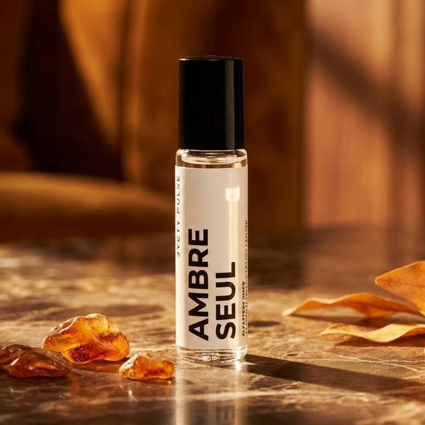 10ml Perfume oil bottle labeled 'Ambre Seul' on a reflective surface with amber-colored stones and leaves.