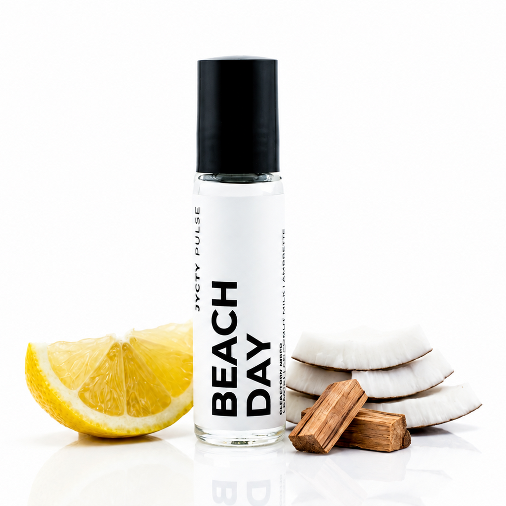 A clear glass roller bottle with a black cap and a white label reading 'BEACH DAY' and 'JYCTY PULSE', styled with a lemon slice, coconut halves, and wooden bark on a white reflective background.
