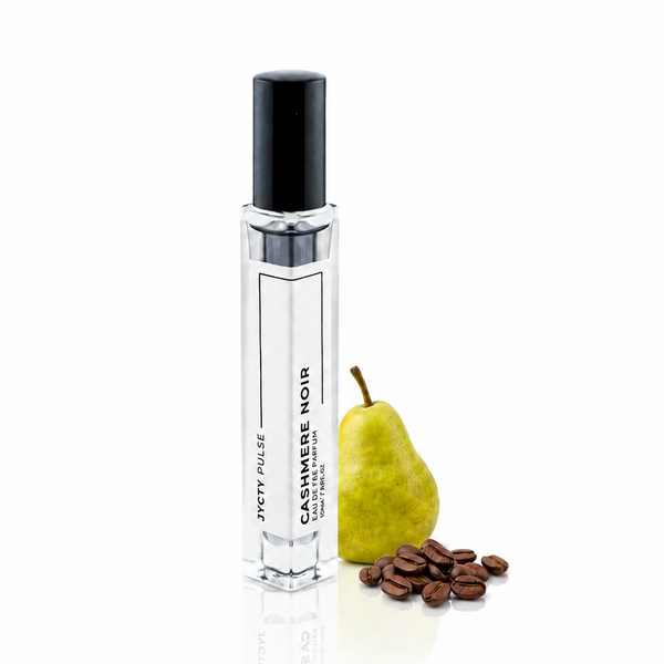 A clear 10ml perfume spray bottle with a black cap, labeled 'JYCTY PULSE Cashmere Noir', standing next to a green pear and scattered coffee beans on a white background.