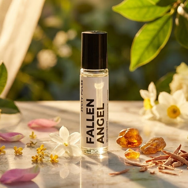 Rollerball perfume oil bottle labeled 'Fallen Angel' surrounded by flowers on a table outdoors.