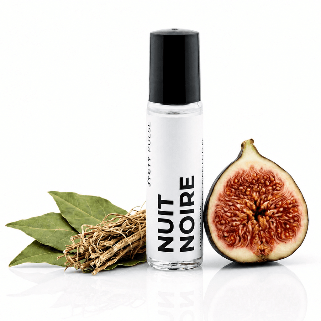 A clear cylindrical spray bottle with a black cap labeled 'NUIT NOIRE' stands on a white reflective surface, styled with green leaves, dried herbs, and a halved fig next to it.