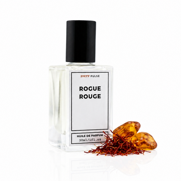A clear glass bottle of Rogue Rouge perfume by jycty Pulse with a black cap and white label, shown on a white background with amber resin and red saffron threads beside it.