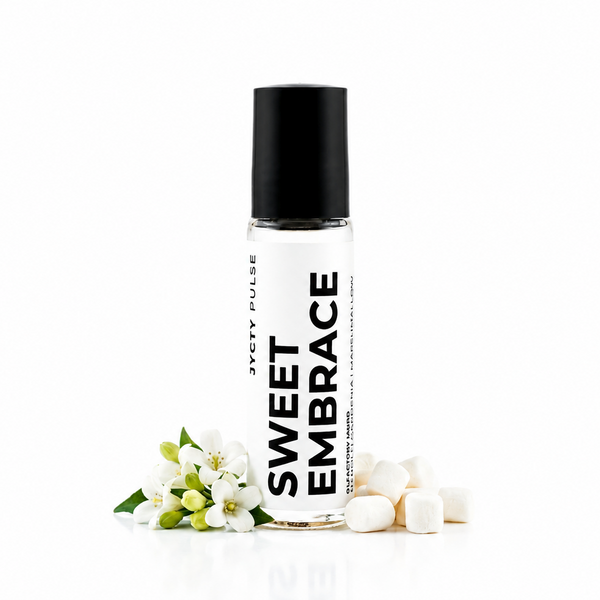 A clear glass roll-on bottle with a black cap labeled 'SWEET EMBRACE' by Scenty Pulse, styled with white blossoms and white cubes on a clean white background.